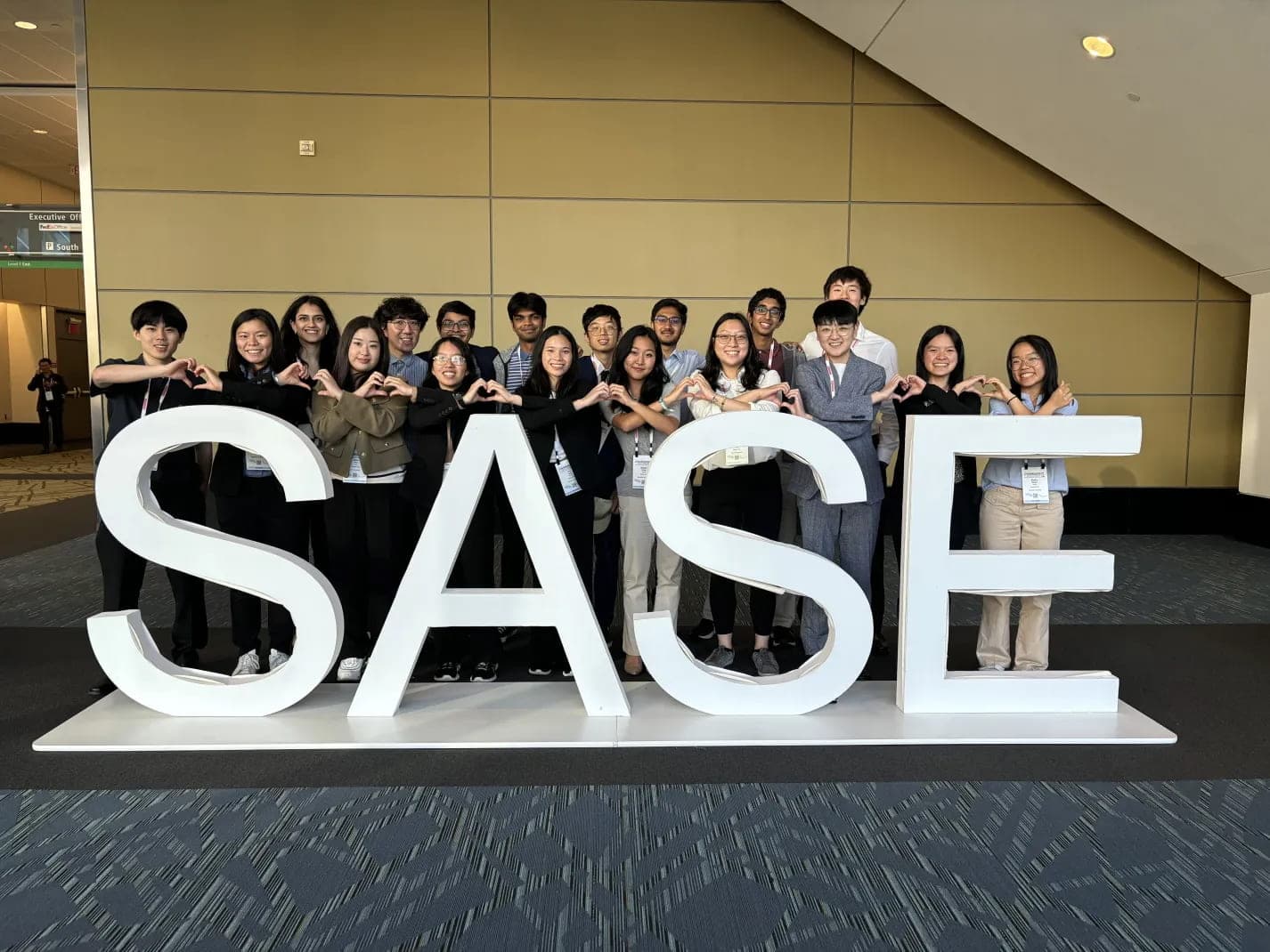 Around twenty SASE GT members posing behind giant SASE letters at the national convention, making heart shapes with their hands.