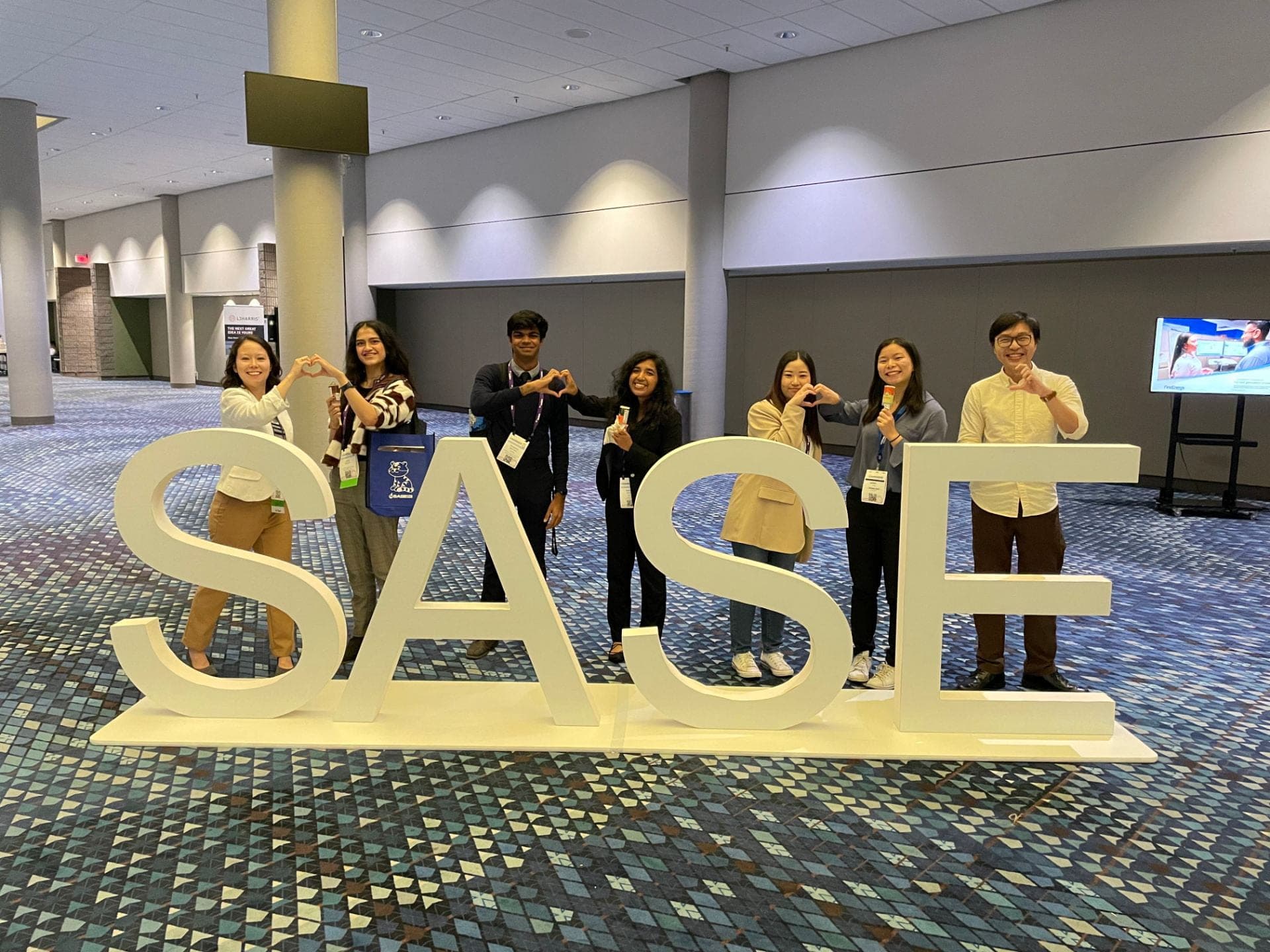 Seven SASE GT members with conference badges standing behind giant SASE letters.
